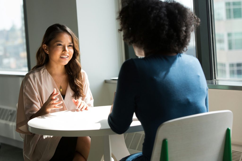 two women having a casual conversation in a well lit office foyer area